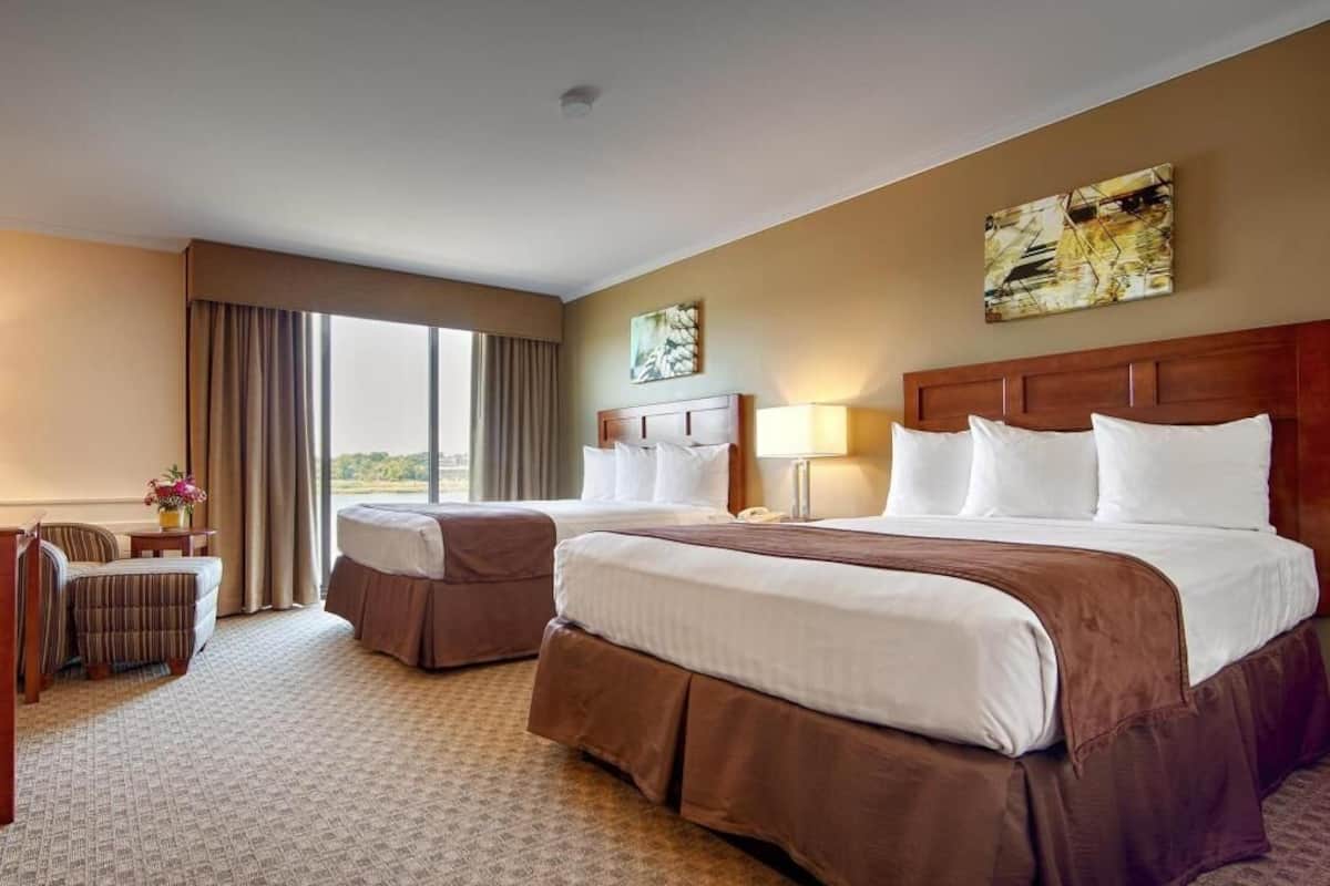 A hotel room with two beds, a desk, a chair, a lamp, and a window with curtains.