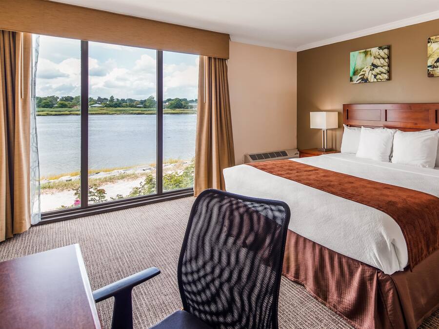 A hotel room with a large bed, a desk, a chair, and a view of a lake.