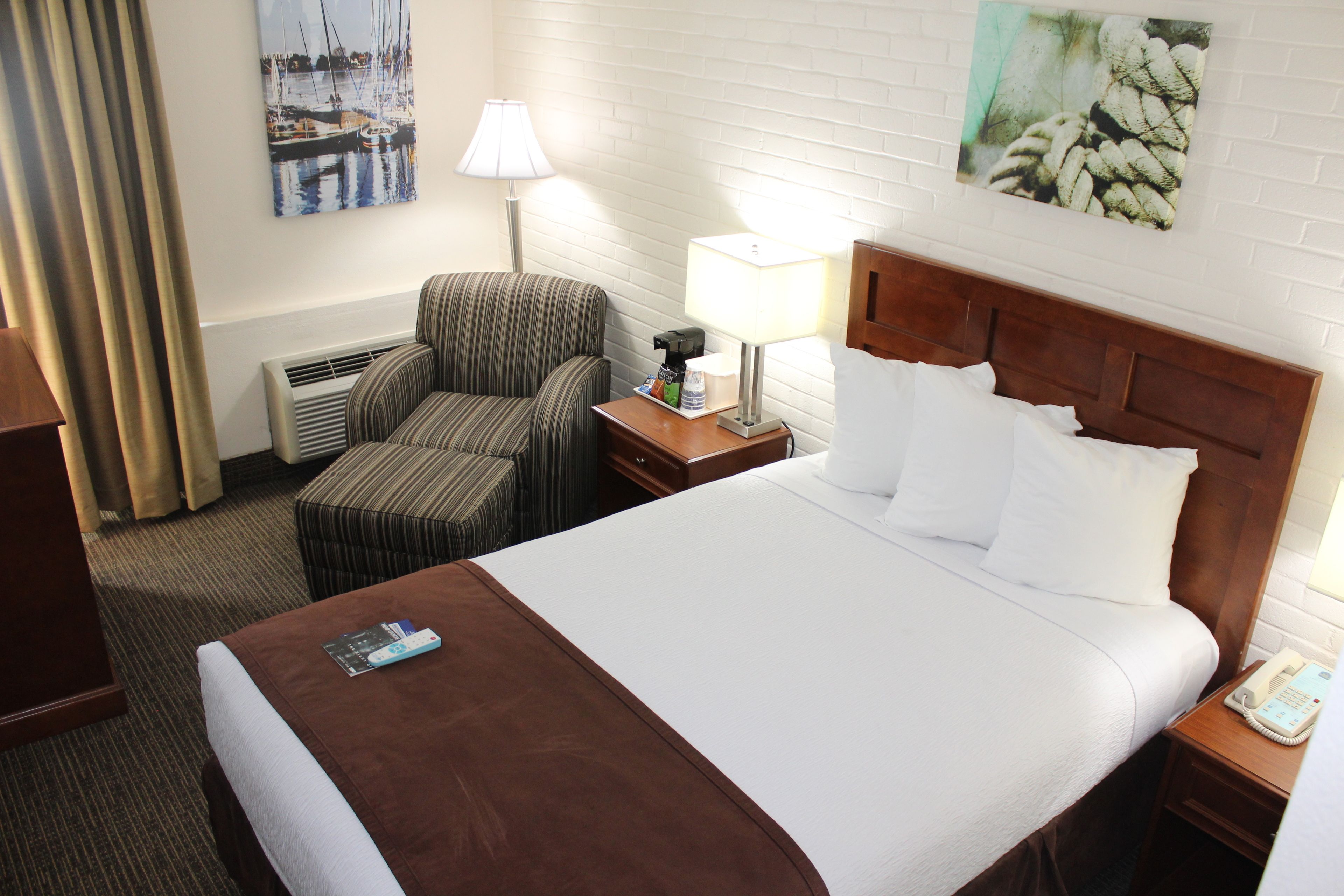 A hotel room with a large bed, a chair, a nightstand with a lamp, and a wall with artwork.