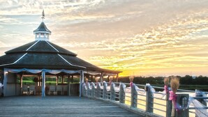 A wooden pier with a gazebo, a view of the sunset, and a river.