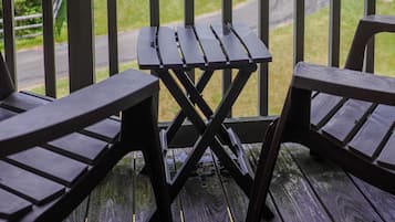 A wooden deck with a table and chairs, overlooking a green landscape and a road.