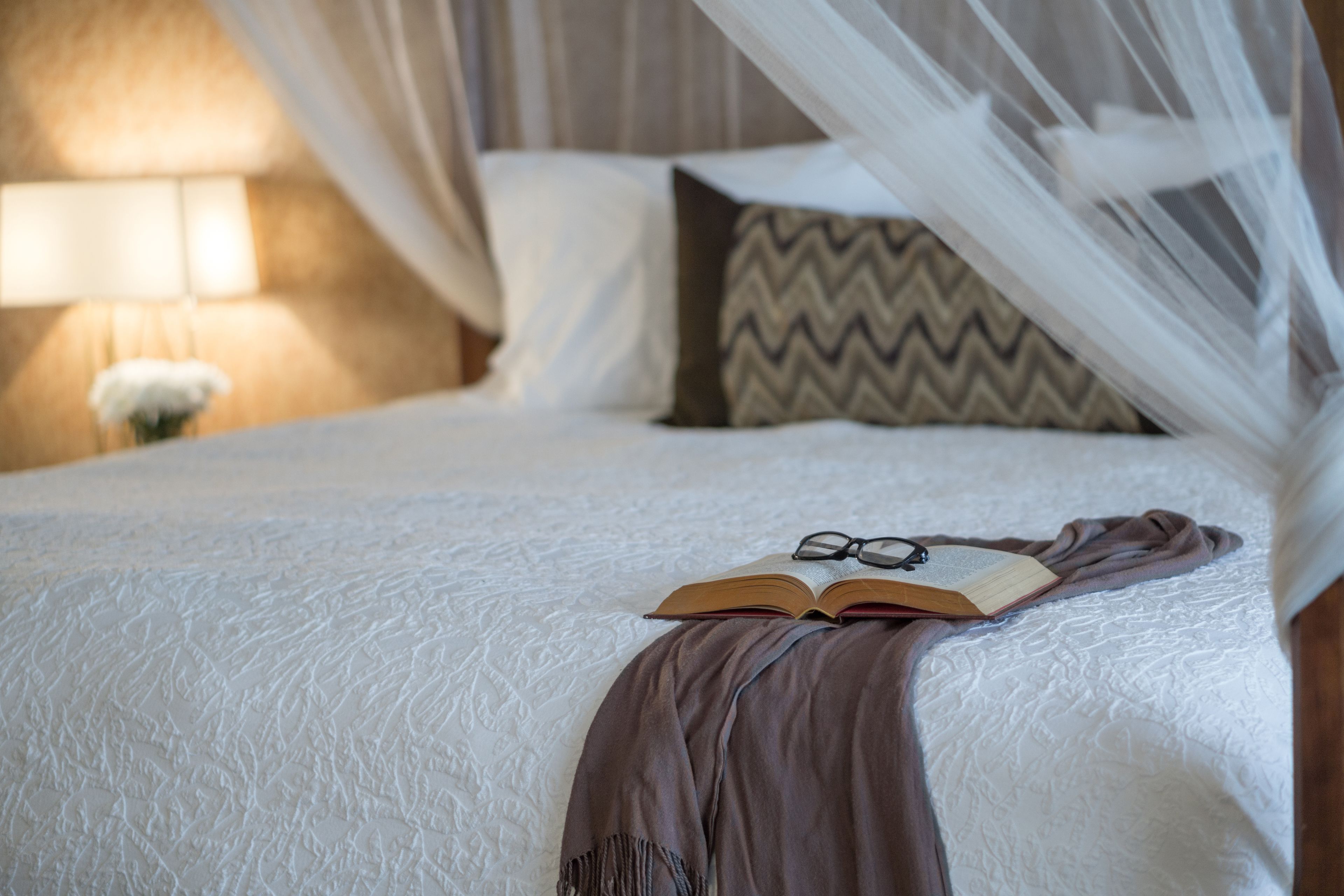 A neatly made bed with a white textured bedspread, a brown throw blanket, and a pair of glasses on an open book.