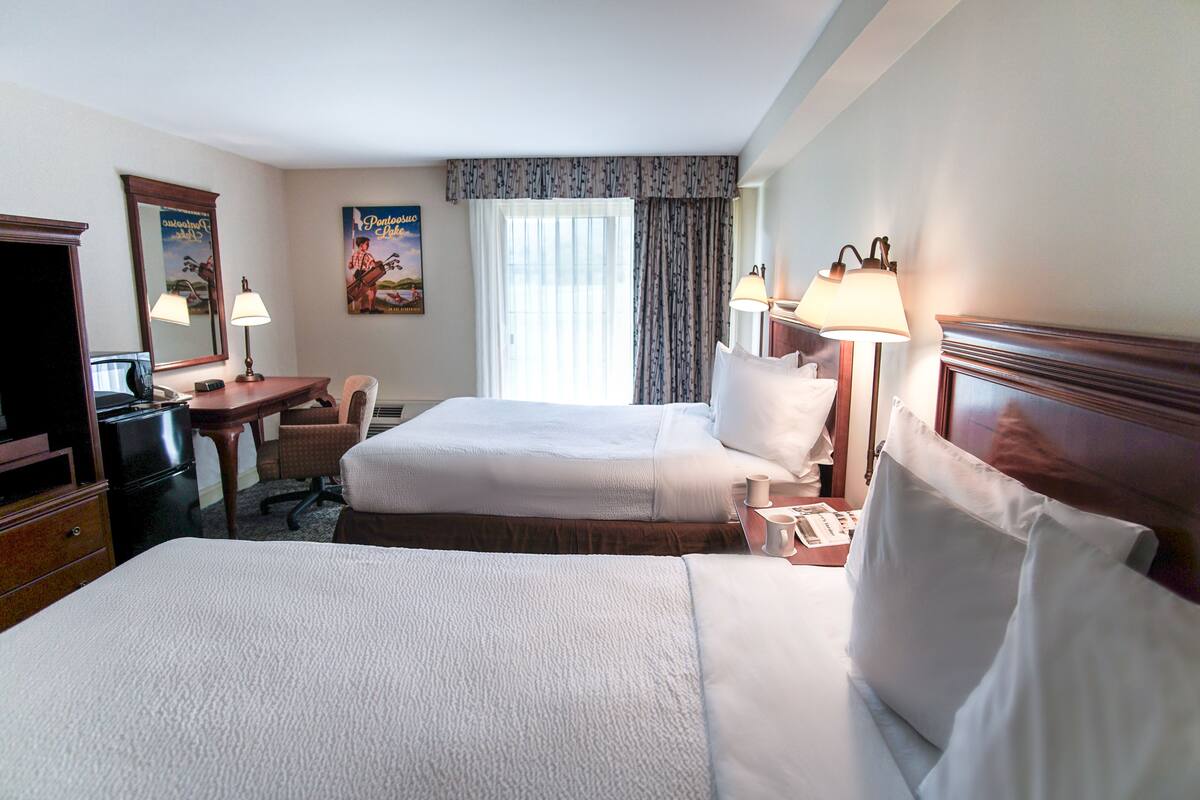 A hotel room with two beds, a desk, a chair, a TV, and a window with curtains.