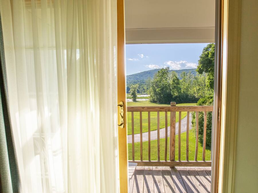 A view from a balcony with a wooden railing, a grassy landscape, and a mountain in the distance.