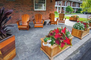 Outdoor wooden chairs and planters with flowers in front of a brick building.