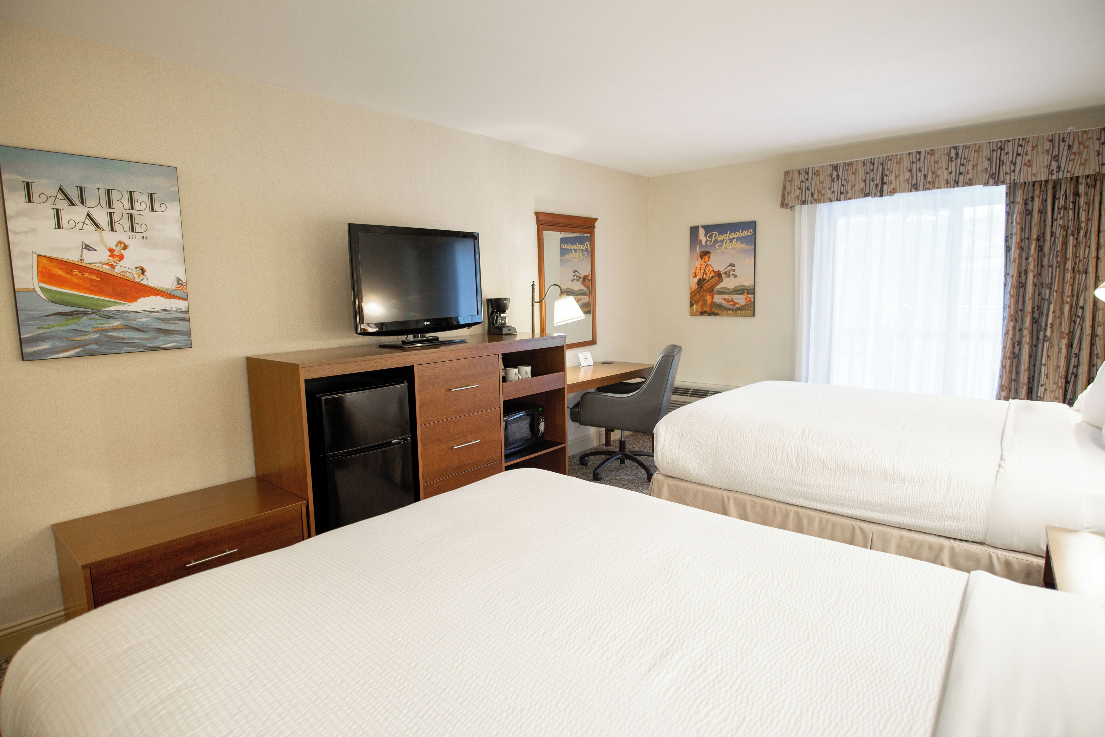 Une chambre d’hôtel avec deux lits, un bureau avec une télévision, un réfrigérateur et un four à micro-ondes.