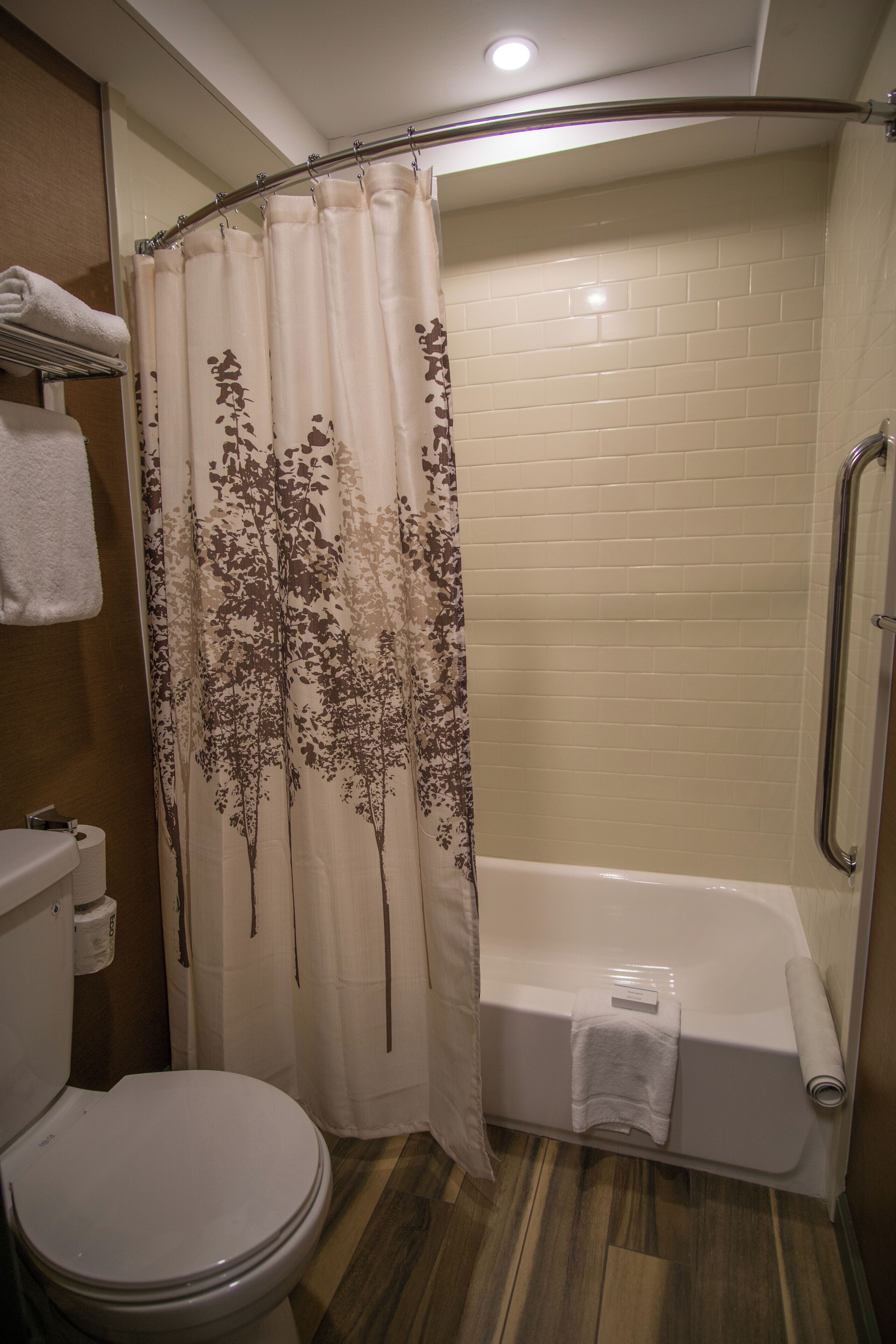 Un baño con inodoro, ducha con cortina de motivos arbóreos y bañera.