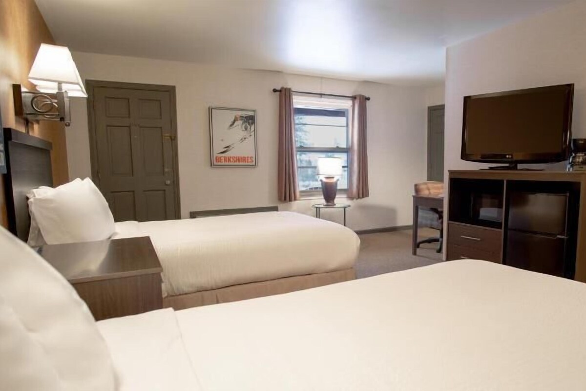 Ett hotellrum med två sängar, ett skrivbord, en tv och ett fönster med gardiner.