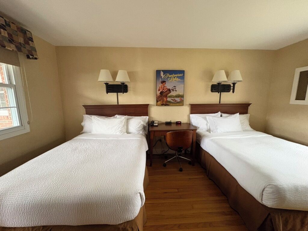 A hotel room with two single beds, a desk, two lamps, and a poster on the wall.