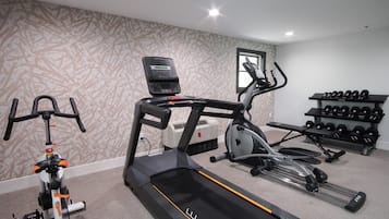A home gym with a treadmill, elliptical, stationary bike, and a set of dumbbells.