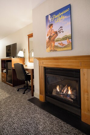 Ein Hotelzimmer mit Kamin, Schreibtisch, Fernseher und einem Poster mit einer Seenlandschaft.