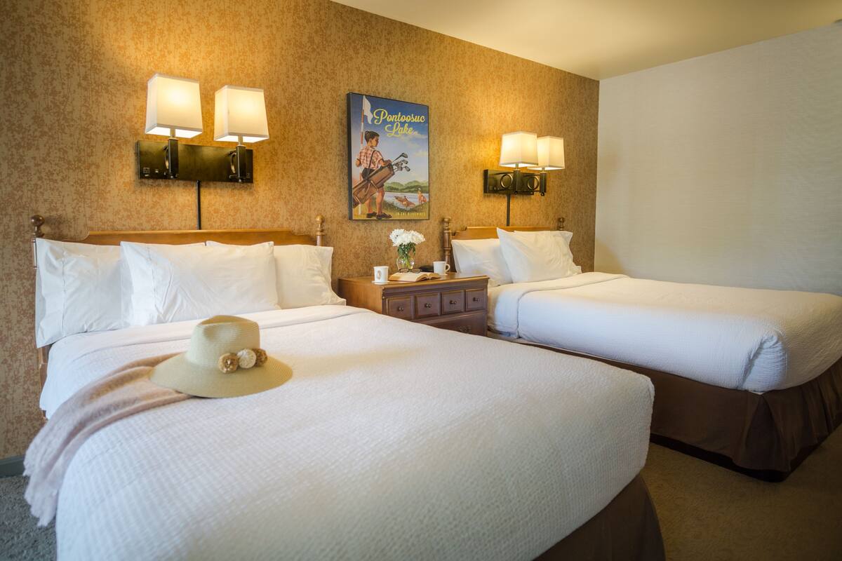 A hotel room with two beds, a nightstand, and wall-mounted lamps.