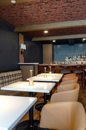 Ein Restaurant mit weißen Tischen, gepolsterten Sitzgruppen und einer Bar.