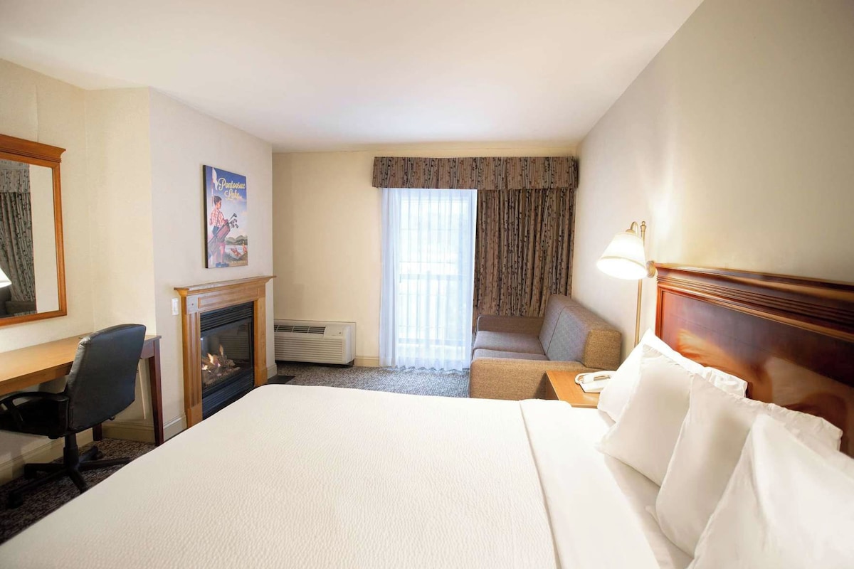 A hotel room with a bed, a desk, a chair, a fireplace, a sofa, and a window with curtains.