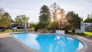 A swimming pool with a surrounding deck, a stone wall, and a building in the background. - The Yankee Inn (Lenox)