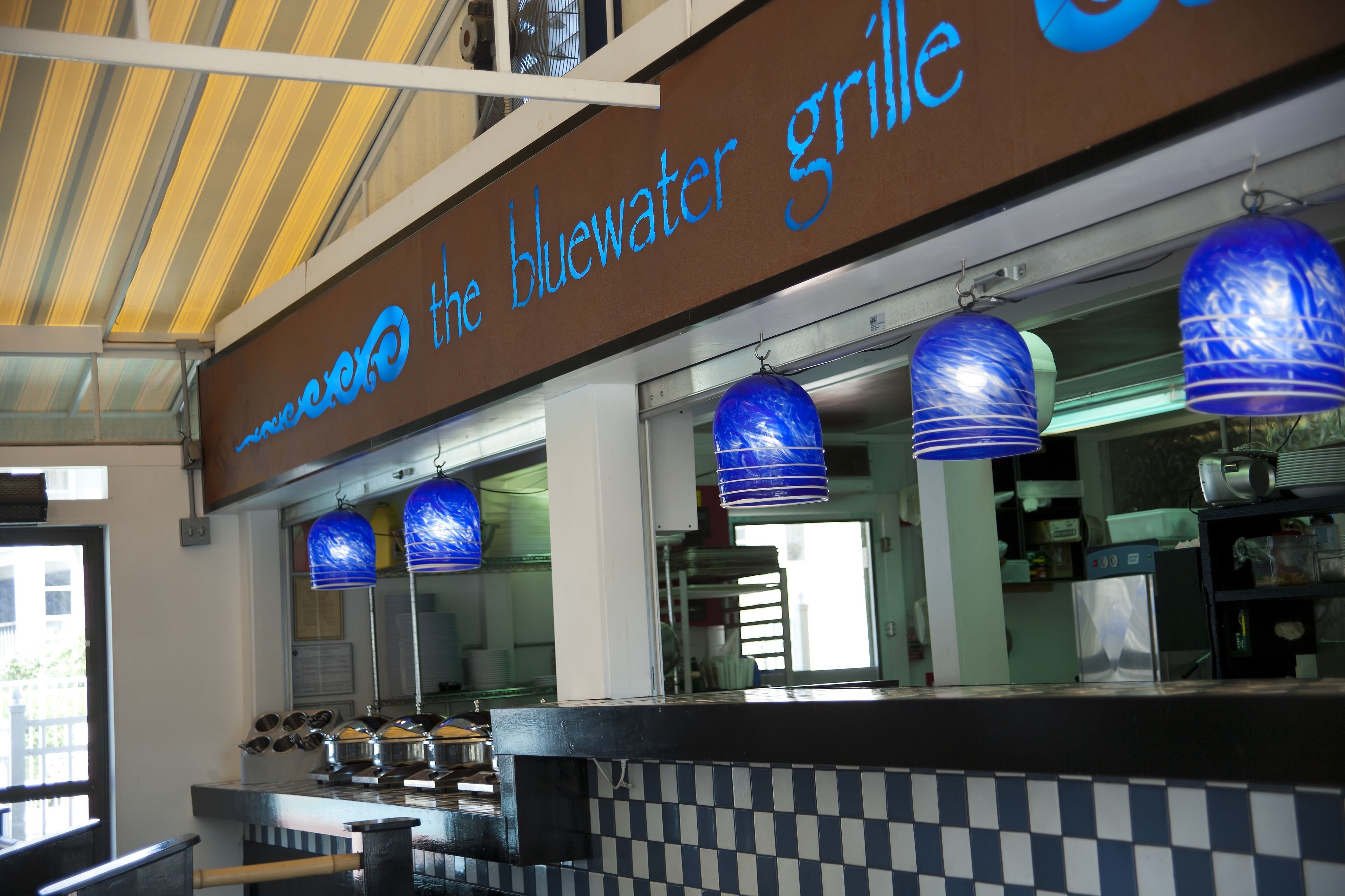 A restaurant with a bluewater grill sign, checkered counter, and blue hanging lamps.