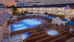 Ein Poolbereich eines Resorts mit mehreren Liegestühlen und Sonnenschirmen, einem Whirlpool und einem großen Gebäude im Hintergrund.