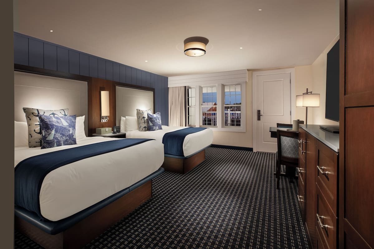 A hotel room with two beds, a large mirror, a desk, and a view of the outside.