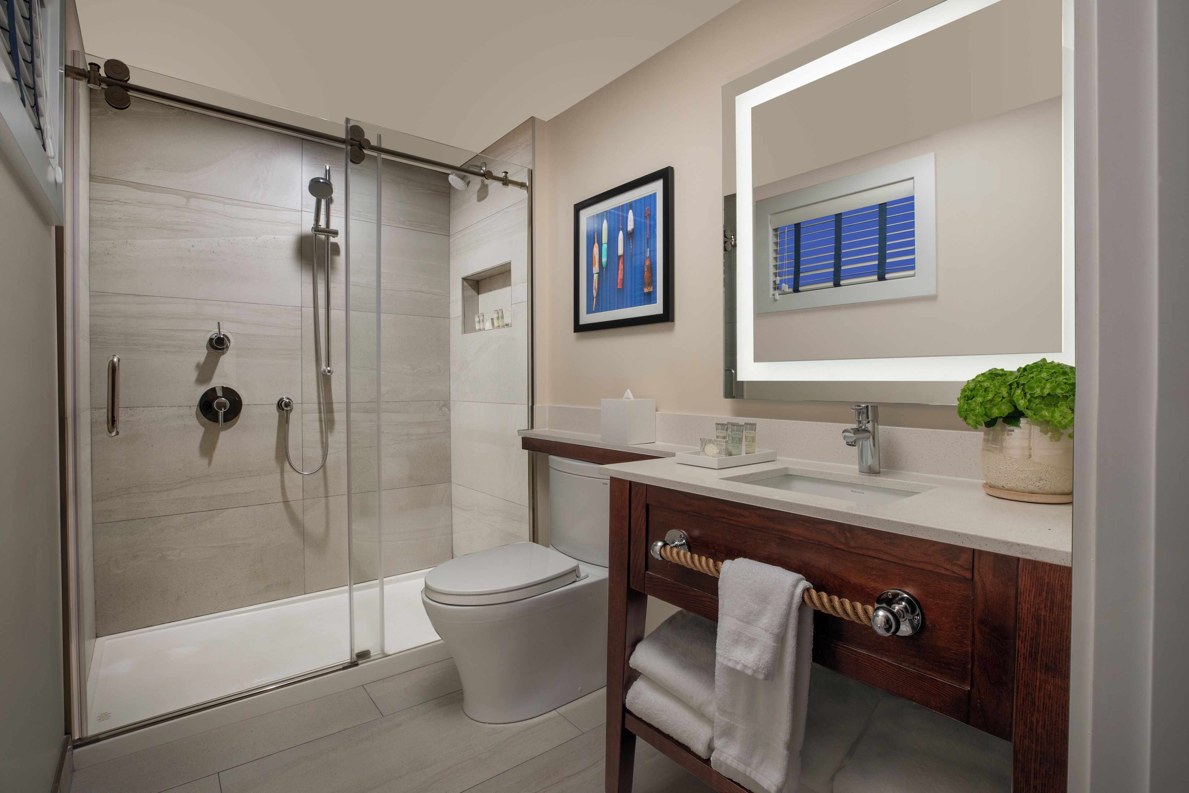 Une salle de bain moderne avec une douche à parois de verre, des toilettes blanches, un meuble-lavabo en bois avec un miroir et une plante en pot.