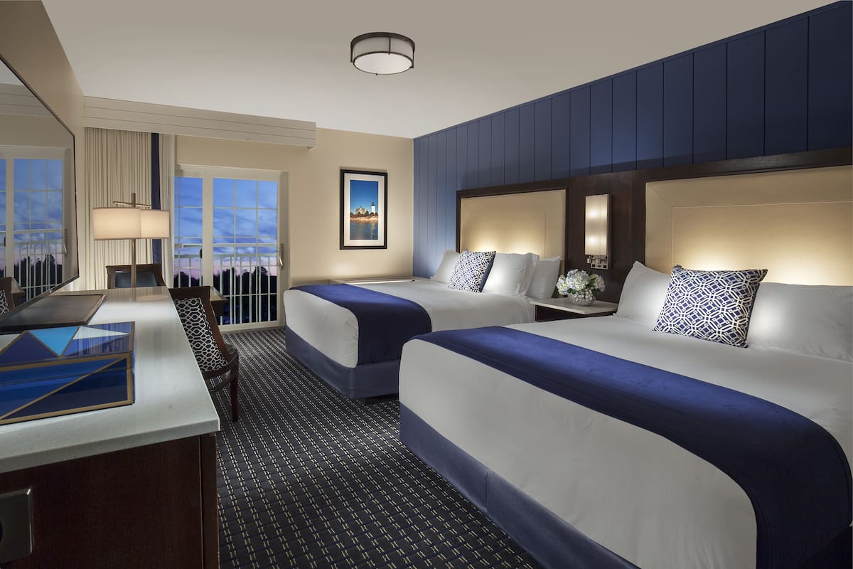 A hotel room with two beds, a desk, and a view of the cityscape.