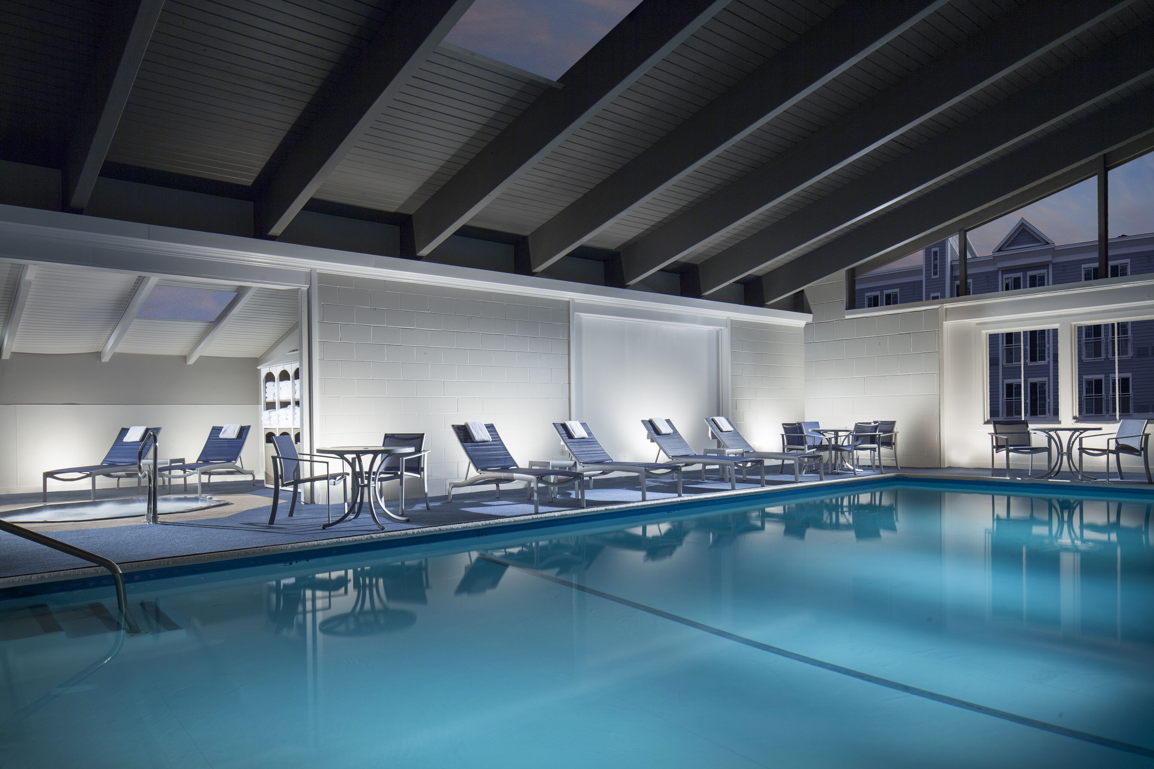 A swimming pool with lounge chairs and tables, a skylight, and a view of a building in the background.