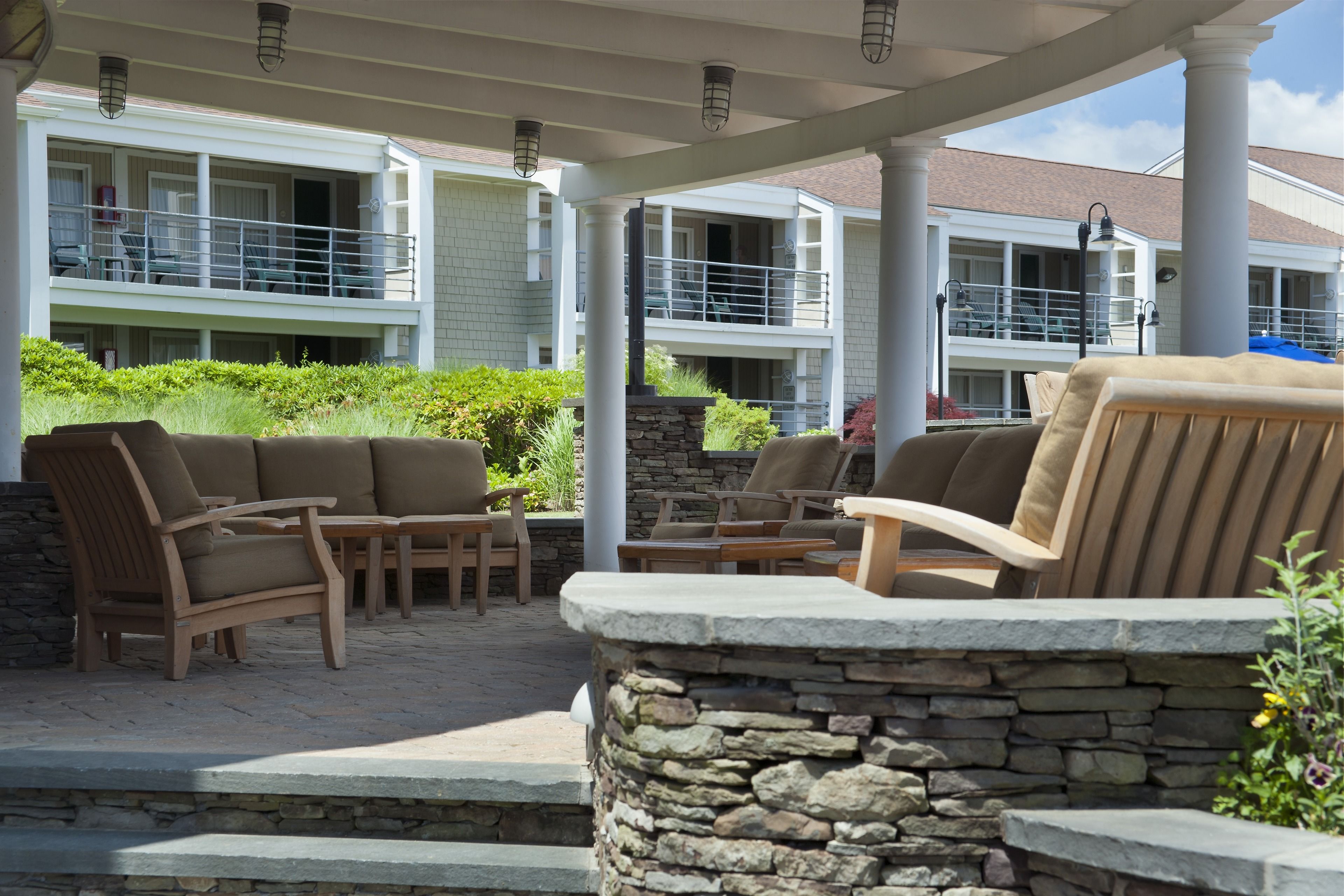 A covered outdoor seating area with stone pillars and a view of a multi-story building with balconies.