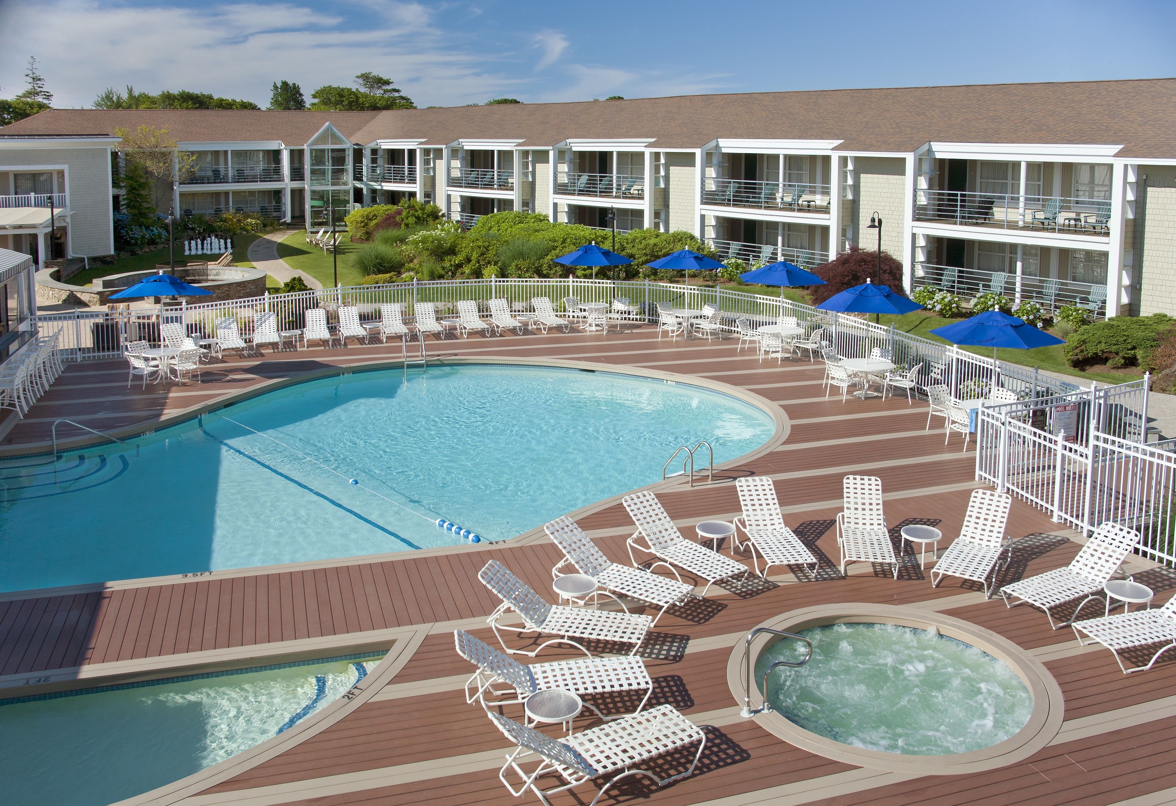 A pool area with lounge chairs and umbrellas, a hot tub, and a building with balconies.