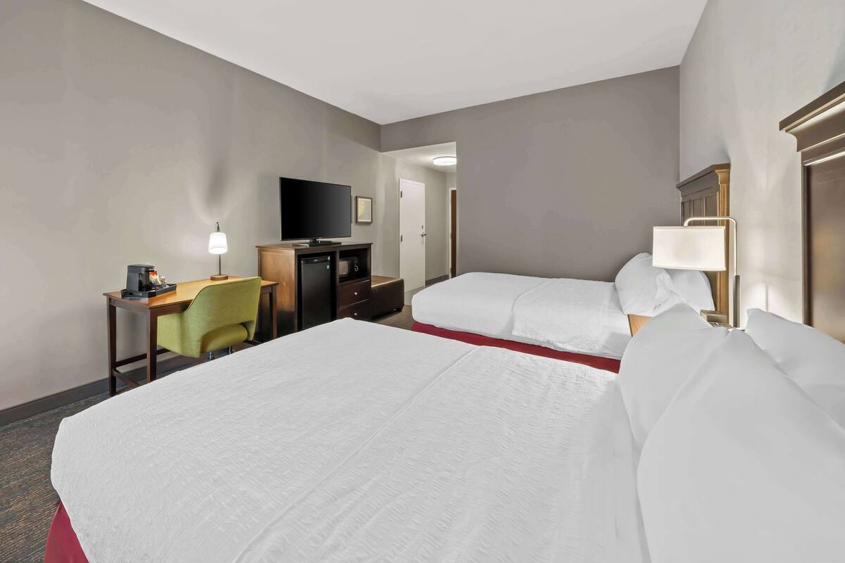 A hotel room with two beds, a desk with a television, a lamp, and a small seating area.