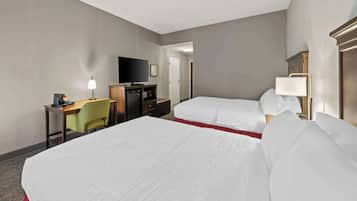 A hotel room with two beds, a desk with a television, a lamp, and a small seating area.