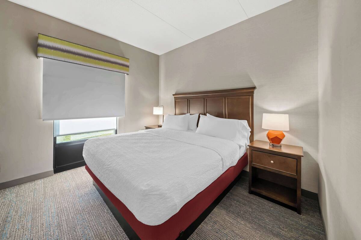 A hotel room with a large bed, two bedside tables with lamps, a window with a view, and a ceiling with a light fixture.