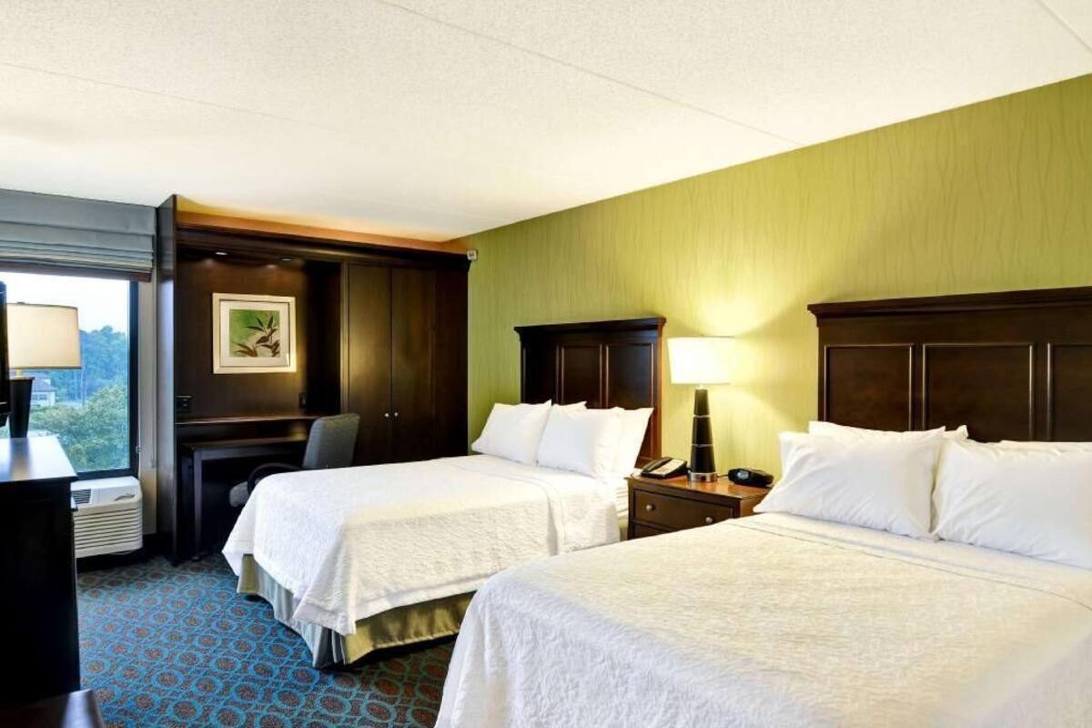 A hotel room with two beds, a desk, a chair, a lamp, and a picture on the wall.