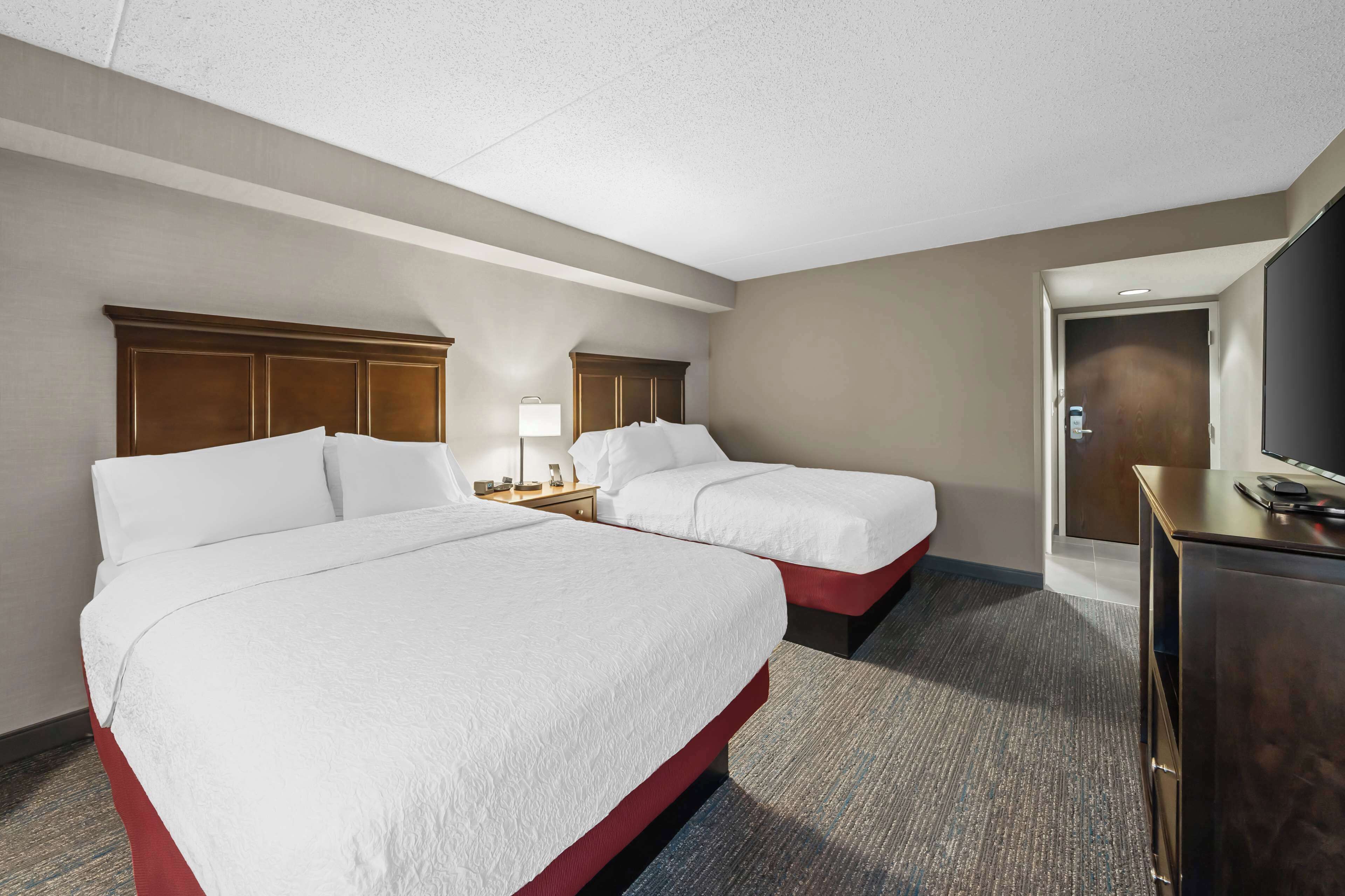 A hotel room with two beds, a desk, a television, and a door.