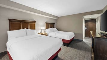 A hotel room with two beds, a desk, a television, and a door.