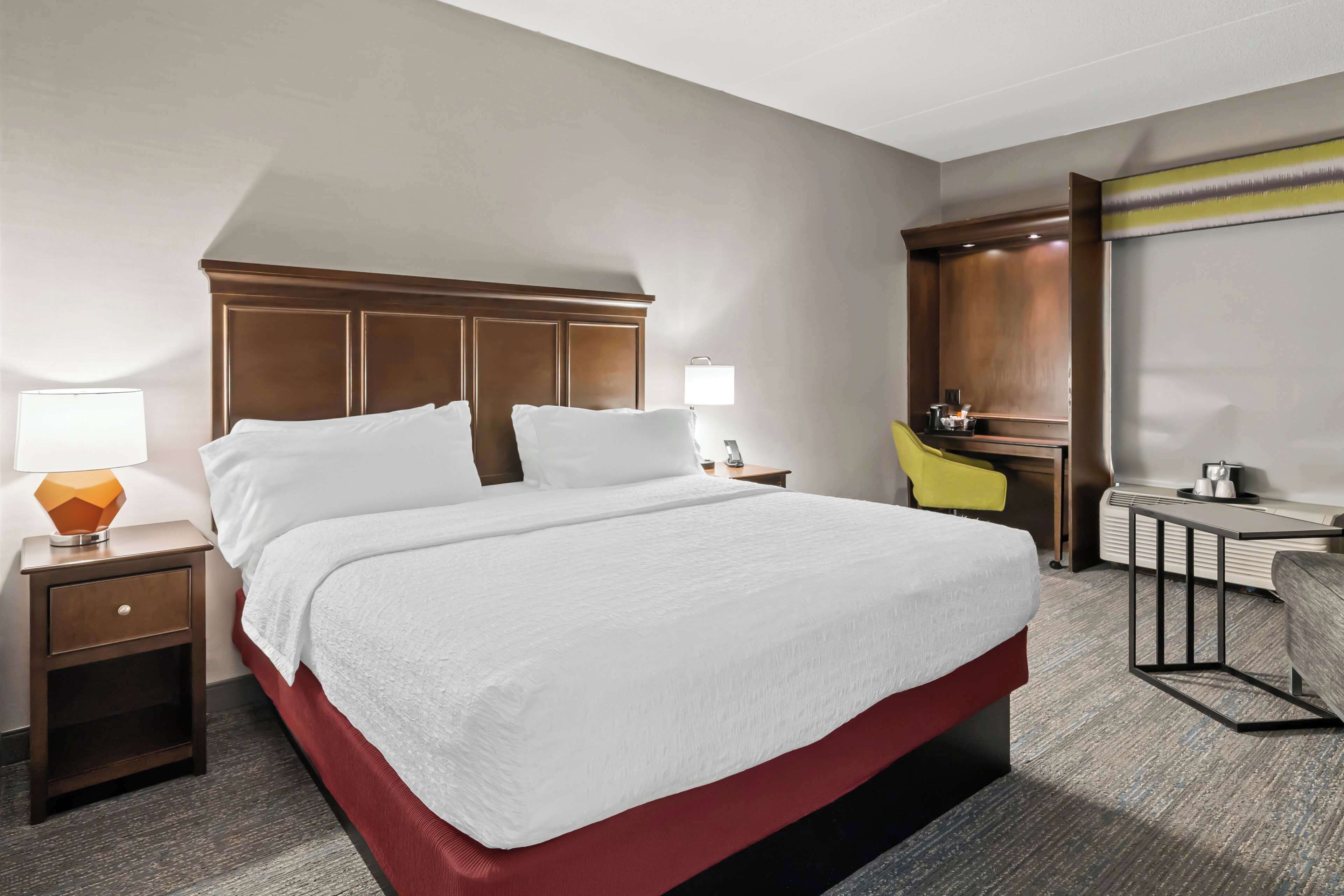 Una habitació d'hotel amb un llit gran, una tauleta de nit amb una làmpada, un escriptori amb una cadira i un mirall.
