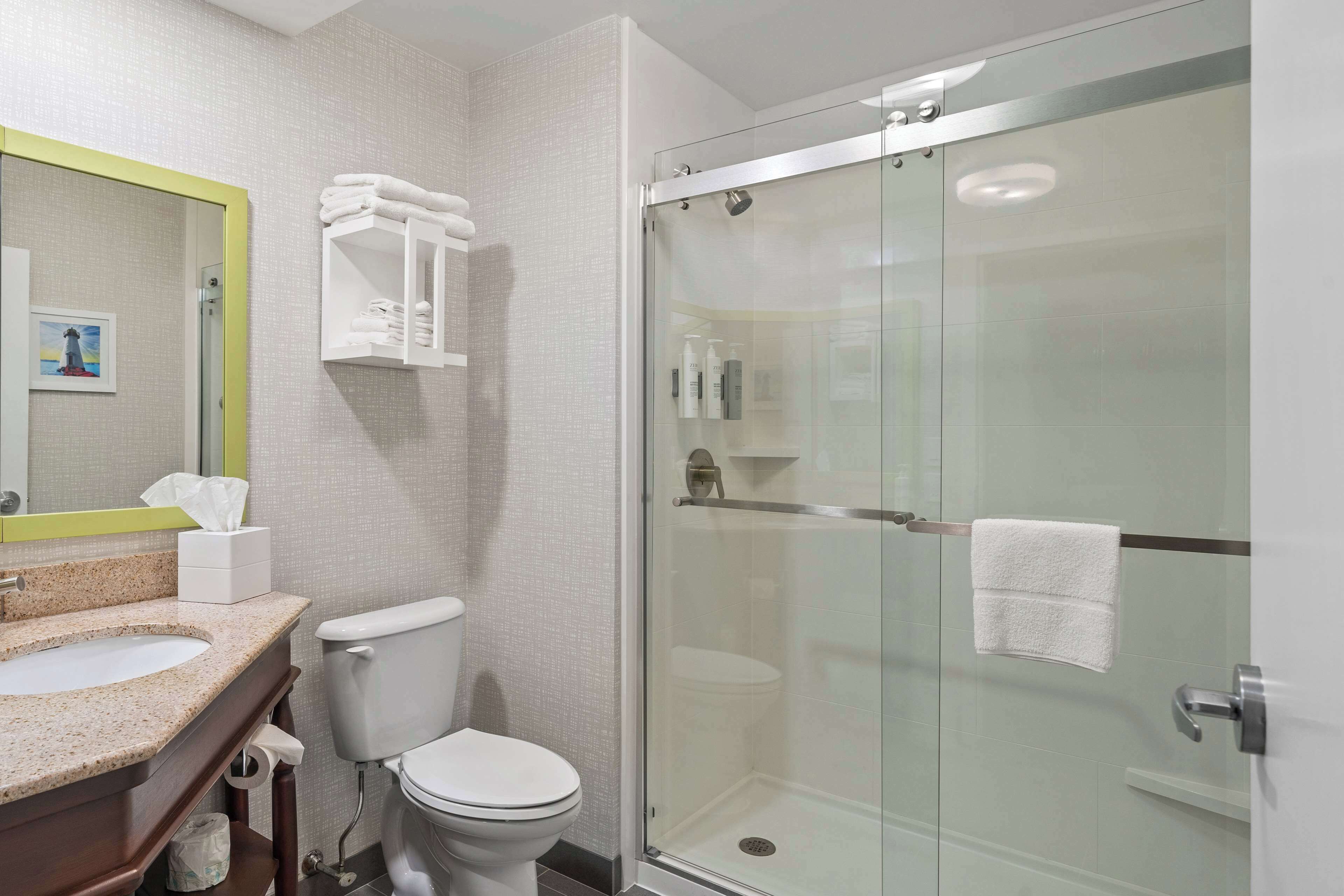 A modern bathroom with a glass-enclosed shower, a toilet, and a sink with a mirror.