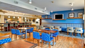 A hotel dining area with multiple tables and chairs, a bar, and a seating area with a patterned wall. - Hampton Inn by Hilton New Bedford/Fairhaven (Fairhaven)