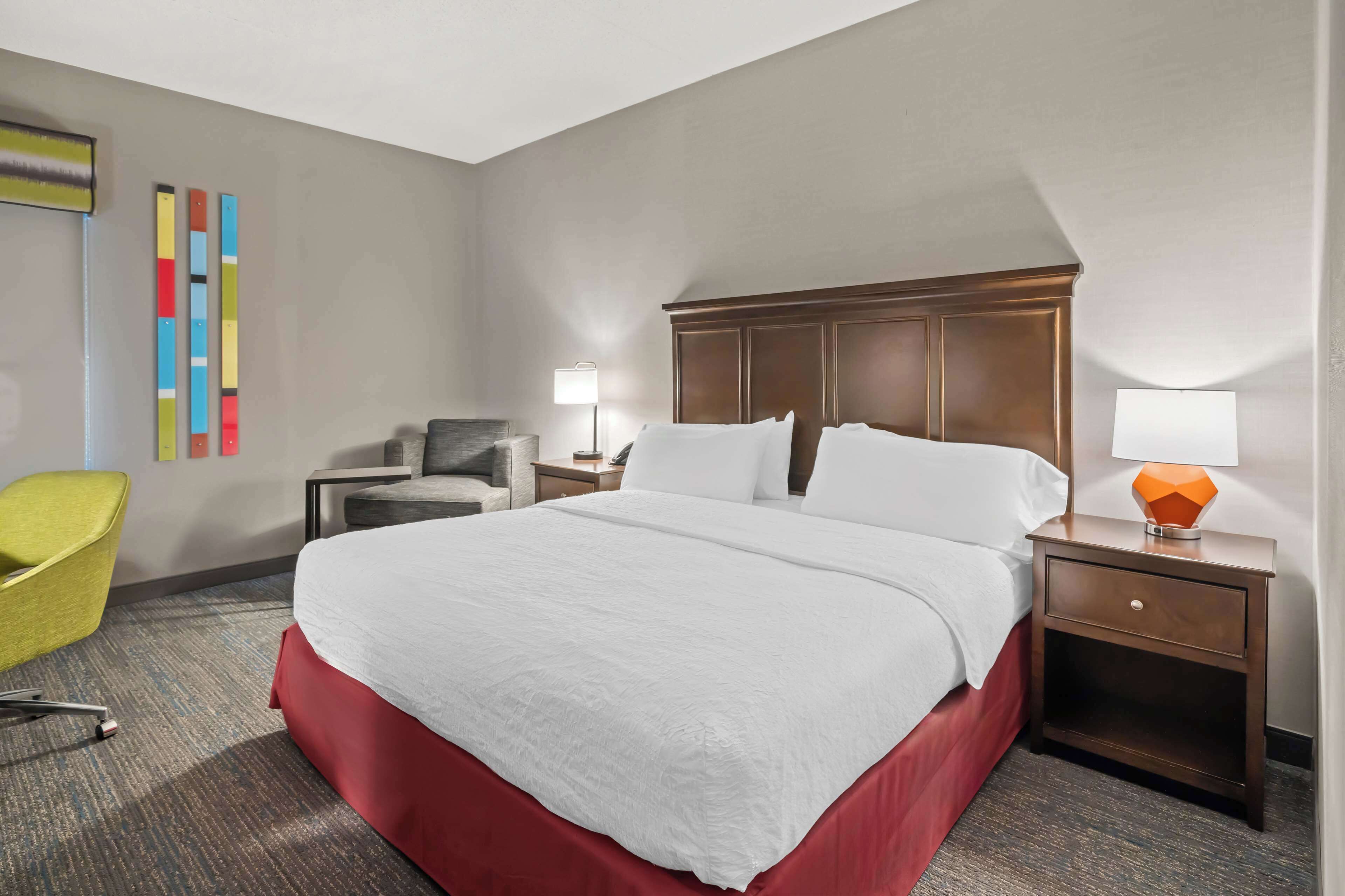 A hotel room with a large bed, a desk, a chair, and a lamp.