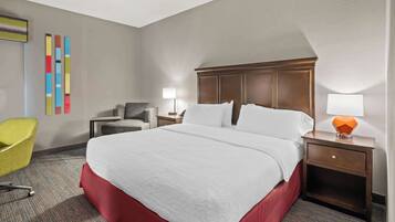 A hotel room with a large bed, a desk, a chair, and a lamp.