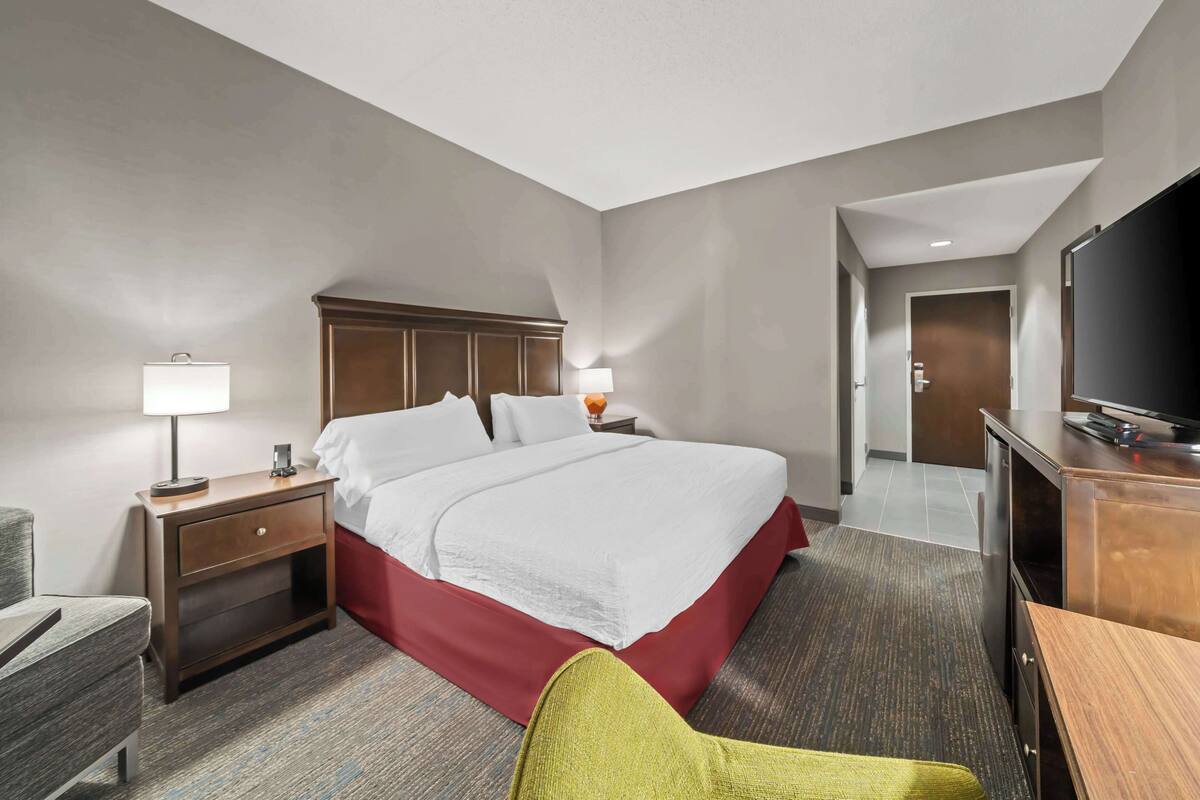 A hotel room with a large bed, a desk, a television, and a chair.