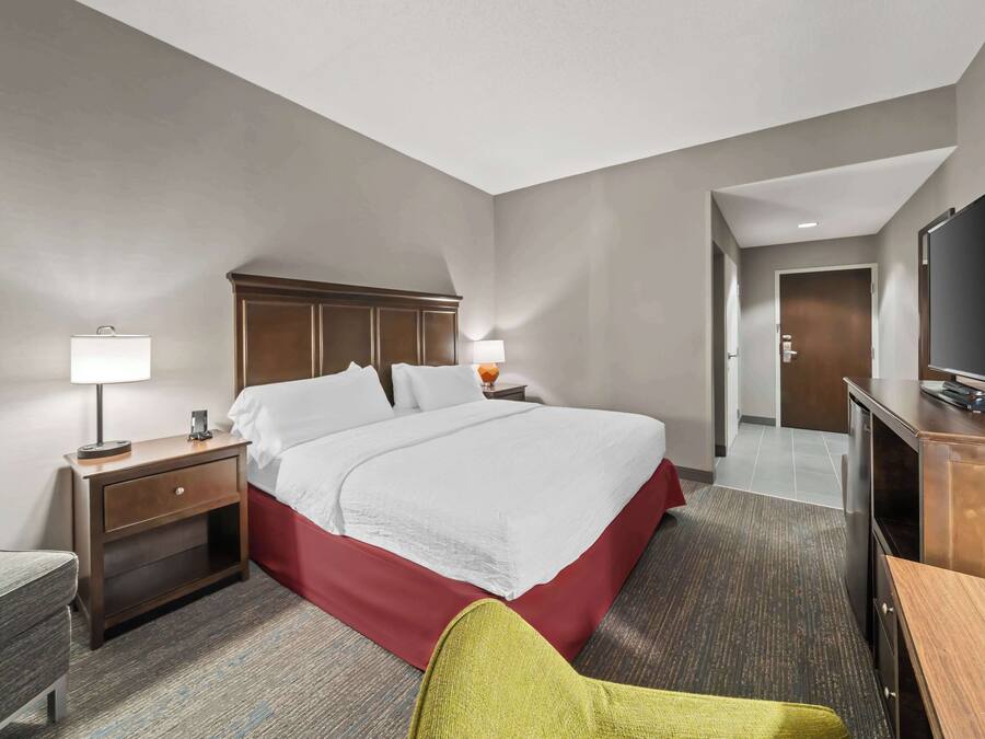 A hotel room with a large bed, a desk, a television, and a chair.