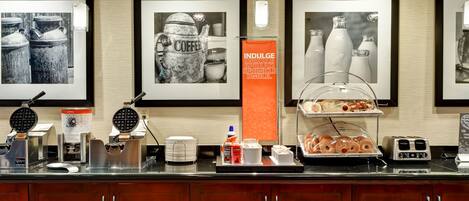 A breakfast bar with waffle makers, coffee machines, and a variety of pastries.