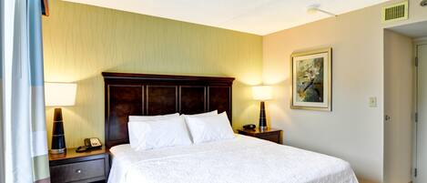 Habitación de hotel con una cama grande, dos mesitas de noche con lámparas, un cabecero de madera, un cuadro en la pared y una puerta a la derecha.