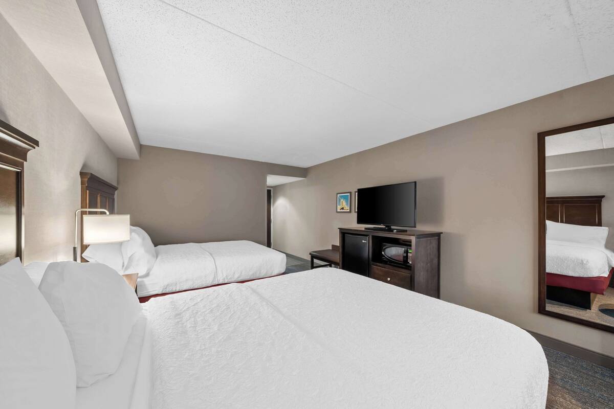 A hotel room with two beds, a television, a desk, and a mirror.
