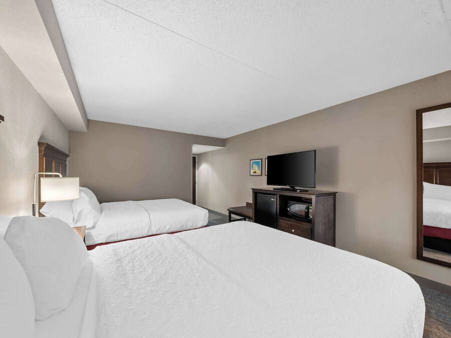 Quarto de hotel com duas camas, televisão, escrivaninha e espelho.