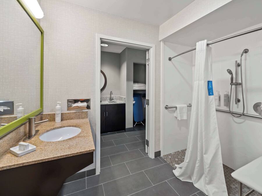 A modern bathroom with a sink, mirror, shower, and towel rack.