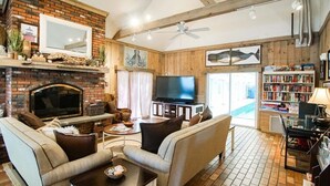 A cozy living room with a brick fireplace, a television, and a bookshelf. - Cape Winds Resort (Hyannis)