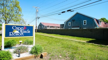 A sign for Cape & Winds Resort with a grassy area and a brick wall in the background.