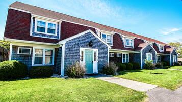A row of townhouses with a central entrance, each with a front porch and a small front yard.