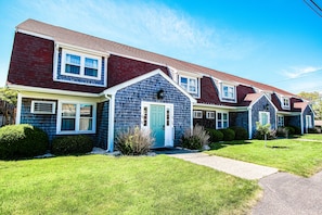 A row of townhouses with a central entrance, each with a front porch and a small front yard.