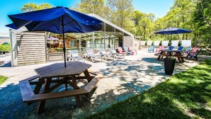 A patio area with picnic tables, umbrellas, and lounge chairs. - Cape Winds Resort (Hyannis)
